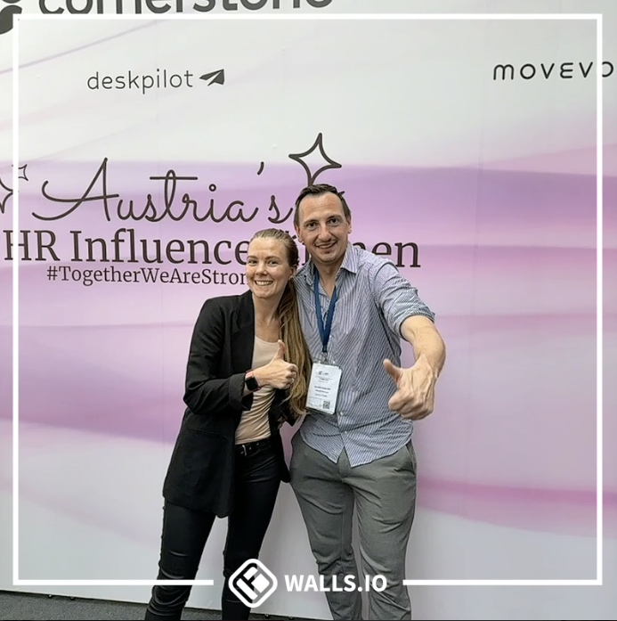 Two HR influencers are giving a thumbs-up in front of a promotional backdrop with various logos and the slogan "#TogetherWeAreStrong" as part of an event.