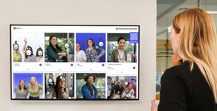 A woman observing a digital screen showing user photos taken at a corporate photo booth, displayed on a social wall in a corporate setting.